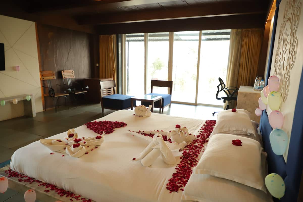 Ett hotellrum med en stor säng, ett skrivbord och en stol. Det ligger rosenblad och en vackert arrangerad handduk på sängen.