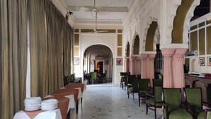 Un long couloir avec des tables et des chaises, des portes en arc de cercle et un ventilateur de plafond.