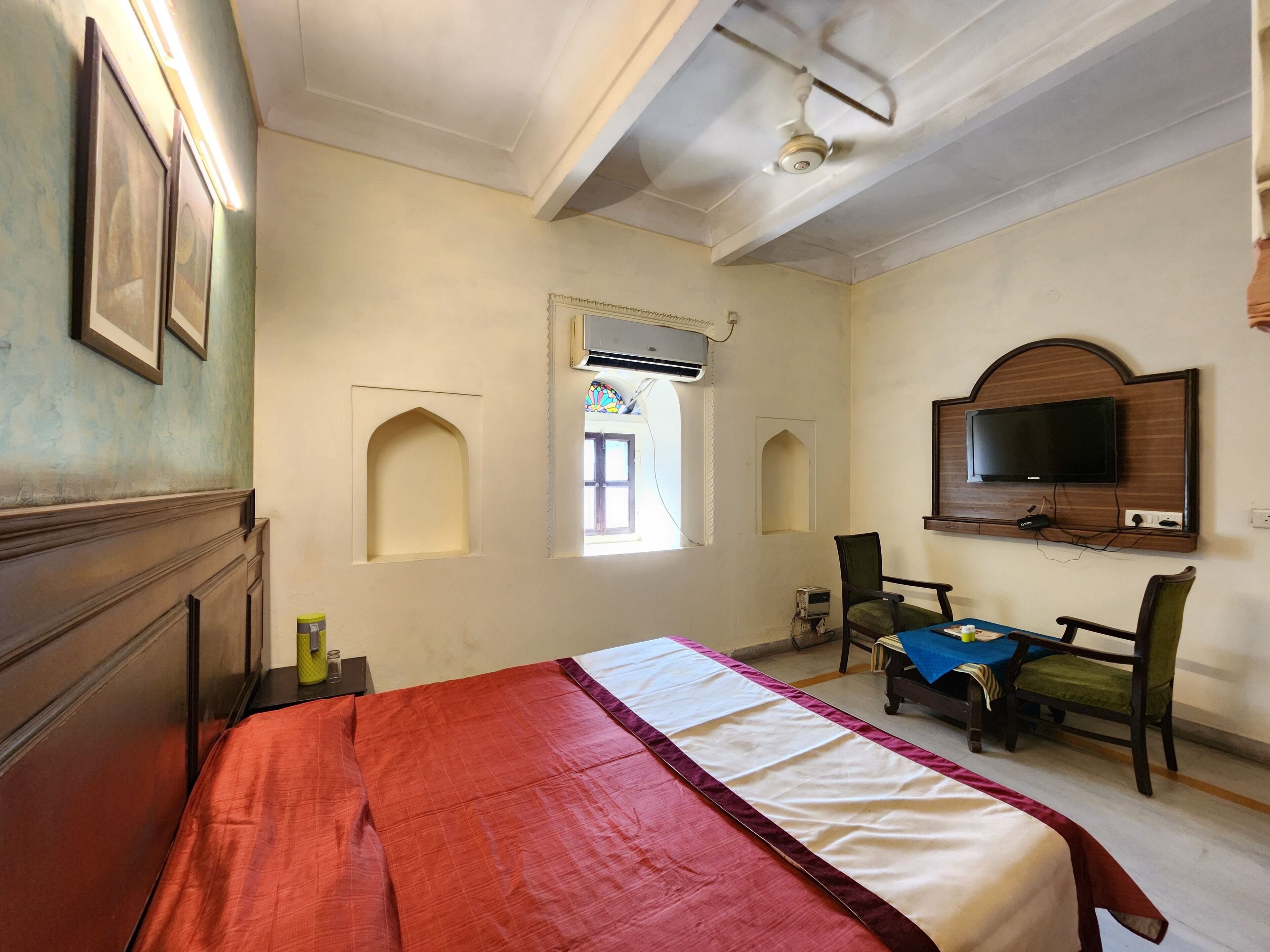Habitación de hotel con cama, televisor montado en la pared y ventana con unidad de aire acondicionado.