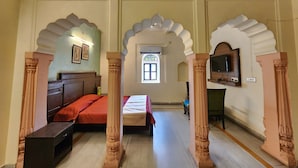 Une pièce comprenant un lit, un bureau et un téléviseur. On y trouve des arches décoratives et une fenêtre ornée de vitraux.