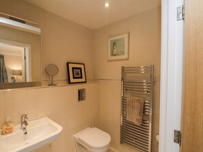A bathroom with a sink, mirror, framed picture, towel rack, and a toilet.