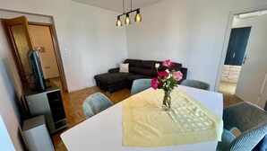 A modern living room with a sofa, a dining table with a vase of flowers, and a TV stand. - Apartment Fruky (Jadranovo)