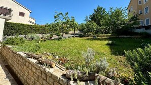 A courtyard with a stone wall, a grassy area, and a tree. - Apartment Fruky (Jadranovo)