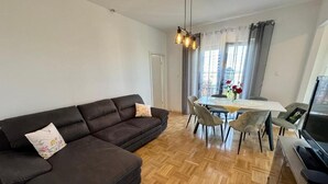 A living room with a dark brown sofa, a dining table with chairs, a television, and a wooden parquet floor. - Apartment Fruky (Jadranovo)