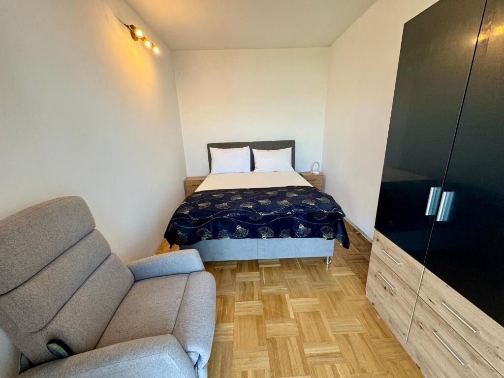 A bedroom with a bed, a grey sofa, a wardrobe, and a light fixture.