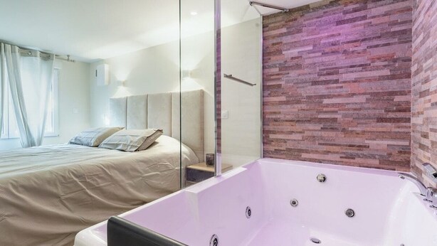 A modern bedroom with a large bed, a glass shower enclosure, and a brick accent wall. - Love Room with Jacuzzi, Le Saccard (Villeneuve-le-Roi)