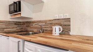 A modern kitchen with a wooden countertop, stainless steel sink, and a built-in microwave. - Love Room with Jacuzzi, Le Saccard (Villeneuve-le-Roi)