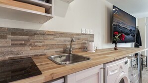 A modern kitchen with a wooden countertop, stainless steel sink, built-in dishwasher, and a flat-screen TV mounted on the wall. - Love Room with Jacuzzi, Le Saccard (Villeneuve-le-Roi)