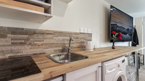 A modern kitchen with a wooden countertop, stainless steel sink, built-in dishwasher, and a flat-screen TV mounted on the wall.