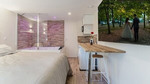 A modern bedroom with a large bed, a shower area, and a small kitchenette. - Love Room with Jacuzzi, Le Saccard (Villeneuve-le-Roi)