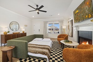 A modern hotel room with a checkered floor, a bed with a leopard print bedspread, a green sofa, an orange armchair, a fireplace, and a ceiling fan.