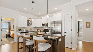 Une cuisine moderne avec des meubles blancs, des appareils en acier inoxydable et un îlot central doté de tabourets de bar.