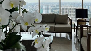 Un salon moderne avec un canapé, une table basse et une vue sur le paysage urbain, visible à travers de grandes fenêtres.