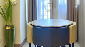 Un espace repas moderne avec une table ronde, des chaises, un vase de fleurs et une vue sur les bâtiments par la fenêtre.