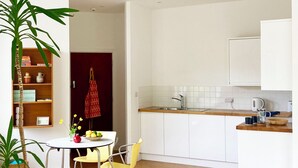 A modern kitchen with white cabinets, a wooden countertop, and a sink. There is a dining table with yellow chairs and a potted plant. - The Old Riverside School House Apt 3 (Hebden Bridge)