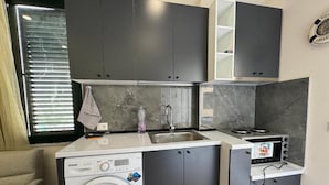 A compact kitchen with grey cabinets, a built-in washing machine, a sink, and a stove. - Tirent Apartment - Cozy Bedrooms Stay by Golem Beach. (Golem)