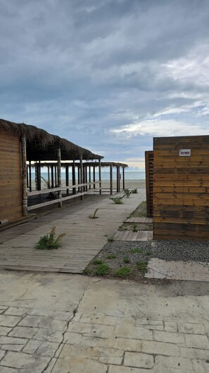 Een houten looppad dat naar een strand leidt, met strandhutten met rieten daken en een houten muur waarop 