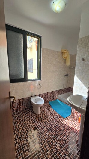 A bathroom with a toilet, bidet, and sink. There is a window with a view of the outside.