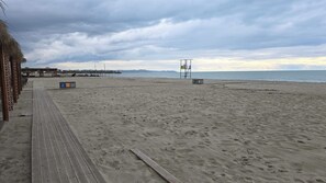 A beach with a wooden boardwalk, lifeguard tower, and a distant pier.