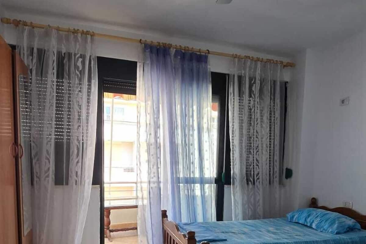 A bedroom with two wooden beds, a ceiling fan, and a view of the outside through a window with sheer curtains.