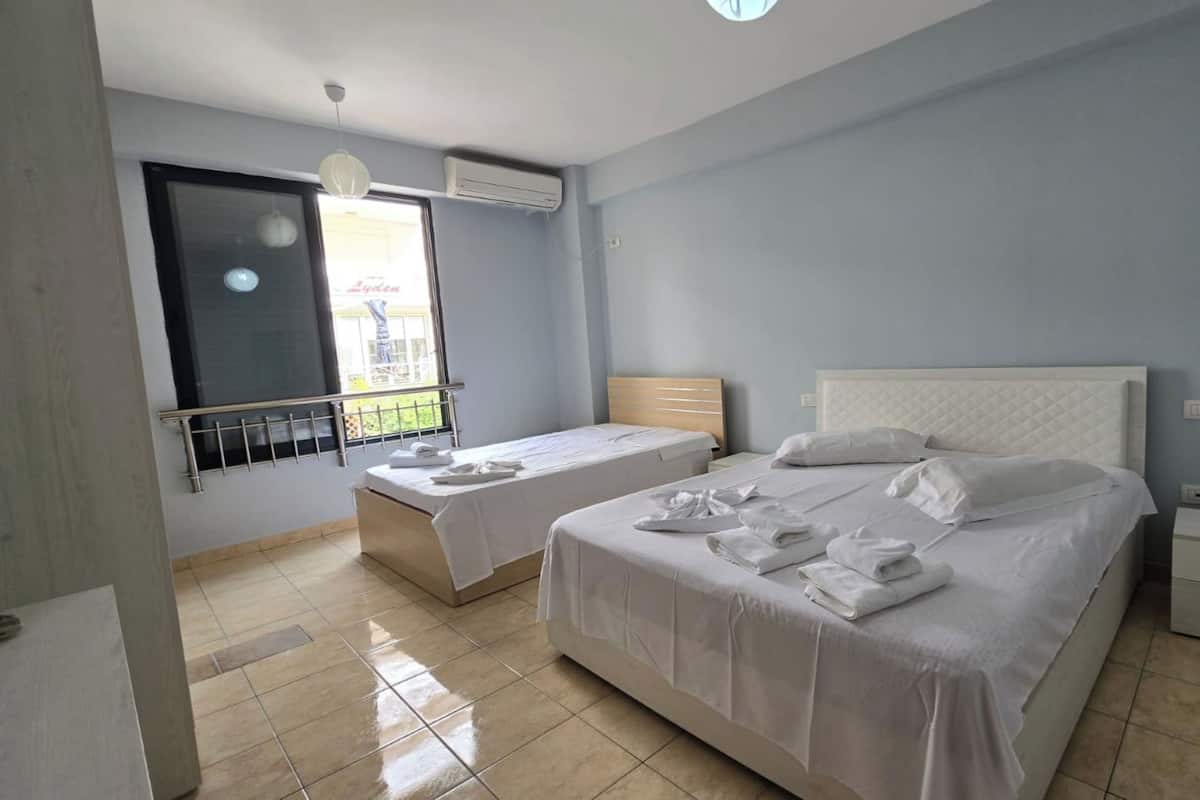 A hotel room with two beds, a window with a view, a hanging light fixture, and a small bedside table.