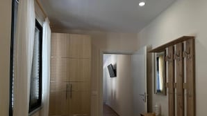 A hallway with wooden flooring, a wardrobe, a bench, and a mirror on the wall. - Tirent Apartment - Cozy Bedrooms Stay by Golem Beach. (Golem)