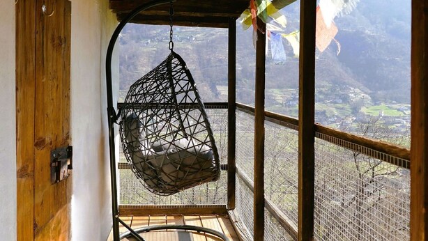 Un fauteuil suspendu dans une pièce au décor rustique, avec vue sur un paysage montagneux.
