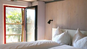 Une chambre à coucher avec un lit, une fenêtre donnant sur un paysage verdoyant et un luminaire fixé au mur.