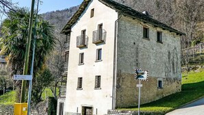 Un bâtiment à deux étages, doté d’une façade en pierre et de nombreuses fenêtres, situé au bord d’une route offrant une vue dégagée sur un paysage montagneux.