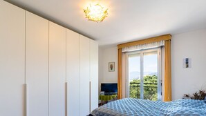 Een slaapkamer met een bed, een bureau, een stoel, een kledingkast en een balkon met uitzicht.