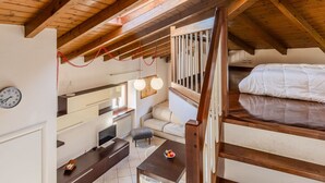 Un dormitorio acogedor en el ático con techo de madera, una cama litera, un escritorio con silla, un pequeño sofá y una mesa de comedor con frutero.
