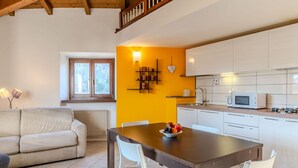 Una sala de estar acogedora con un sofá y una mesa de comedor preparada para cuatro personas. Se ve una cocina con armarios blancos y un microondas al fondo.