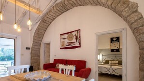 A cozy dining area with a wooden table, white chairs, and a red sofa. A decorative plate is on the table, and a painting hangs on the wall. - Wonderful private villa for 6 people with WIFI, TV, patio and pets allowed (Aglientu)