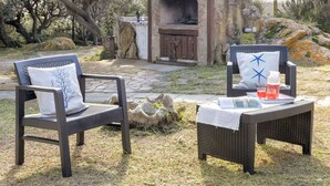 Two wicker chairs with white cushions, a small table with a white cloth, and a stone-built outdoor kitchen with a chimney. - Wonderful private villa for 6 people with WIFI, TV, patio and pets allowed (Aglientu)