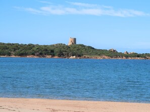 Uitzicht op de kust met een kasteel op een heuvel, helderblauw water en een zandstrand.