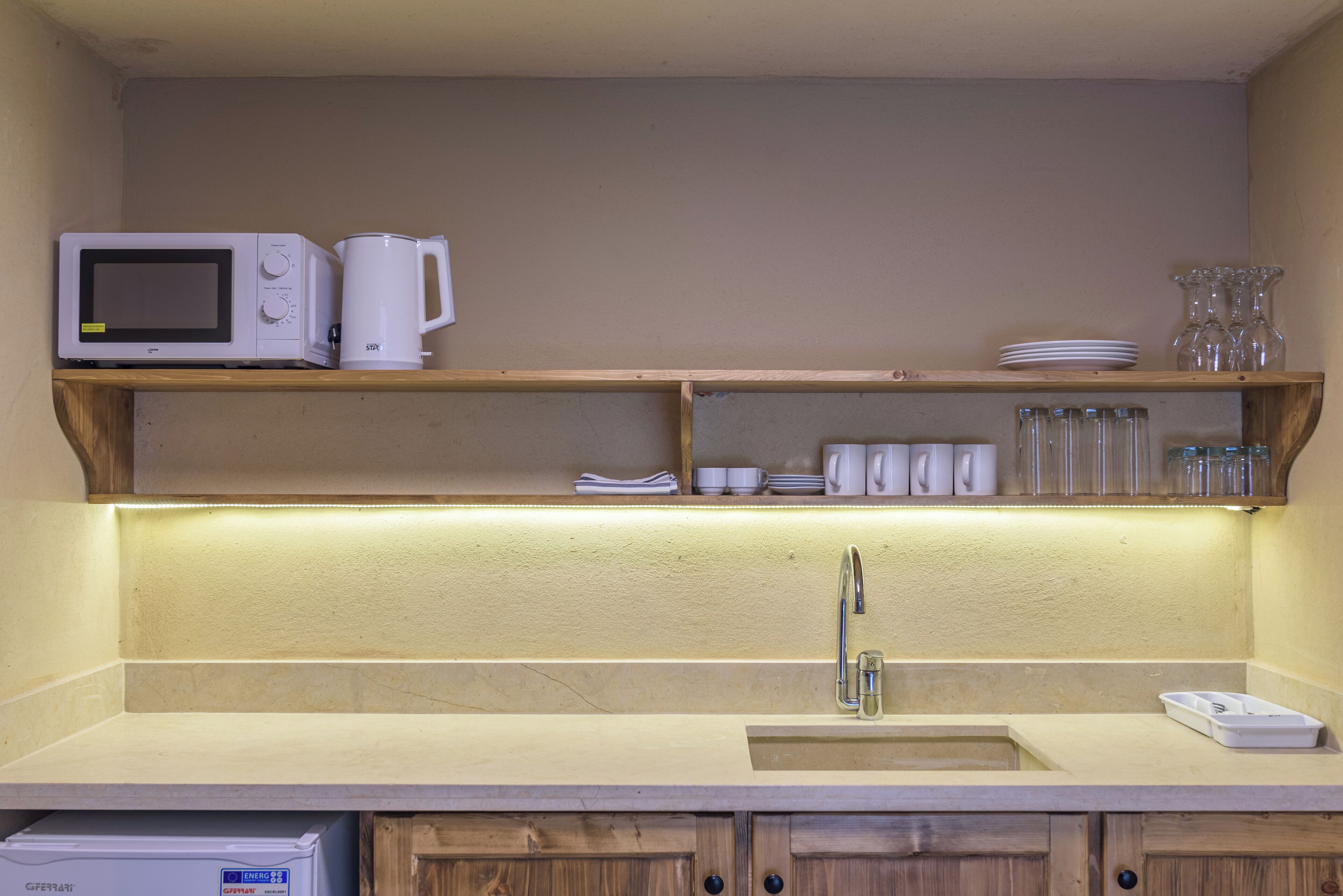 Una cocina con microondas, cafetera y estantes con vajilla y vasos.