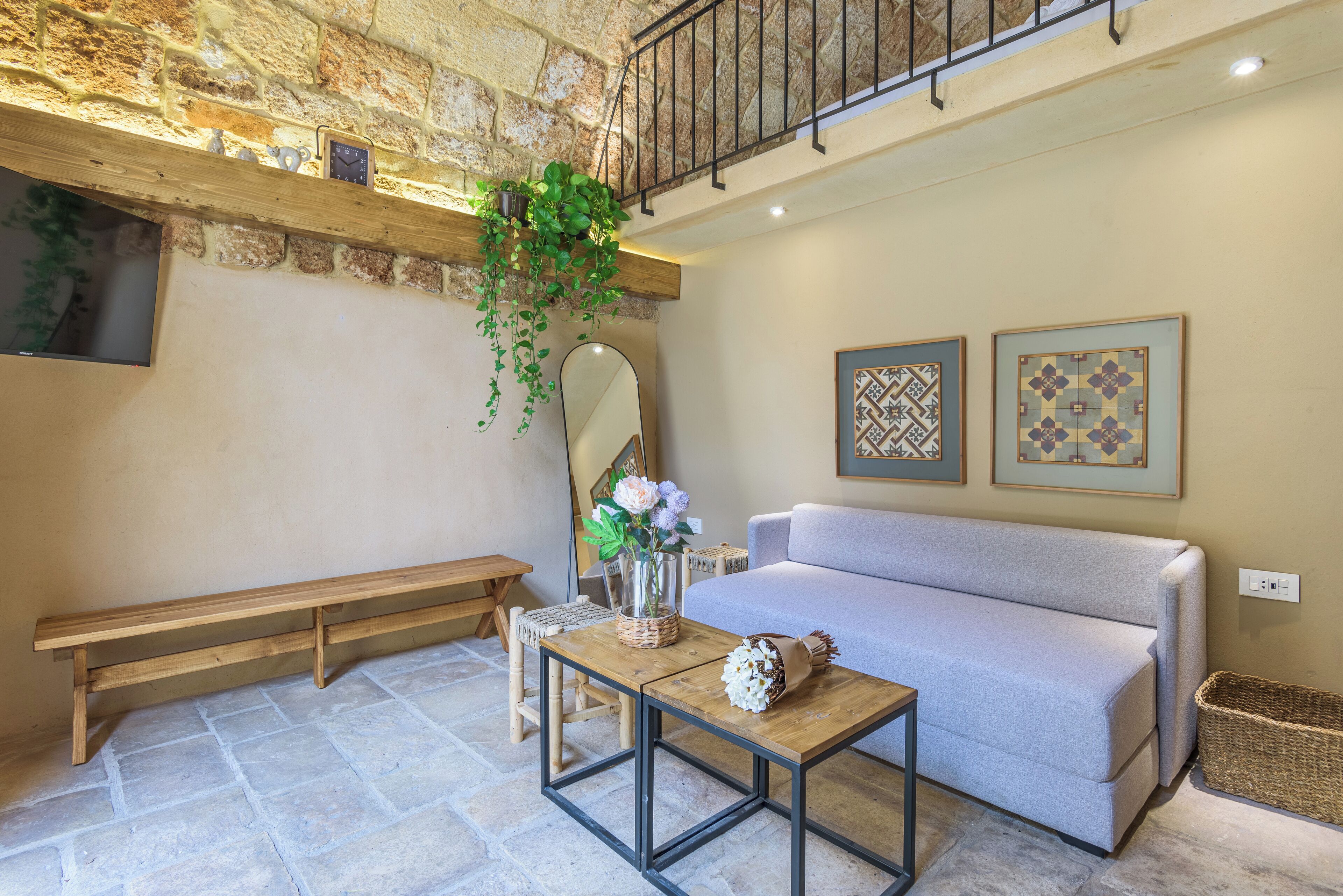 Una sala de estar acogedora con una pared de piedra, un banco de madera, un sofá, una mesa de centro con un jarrón de flores y una planta colgante.