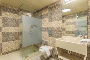 A bathroom with mosaic tile walls, a glass shower enclosure, a toilet, and a sink with a towel on it. - Casa Batroun Lofts (Batroun)