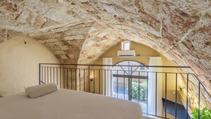 Ein Schlafzimmer mit einem großen Bett, einer gewölbten Steindecke und einem Balkon mit Geländer.