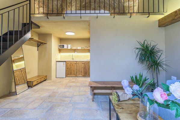 Un salón amplio con un banco de madera, una mesa de comedor con un florero y una cocina al fondo.