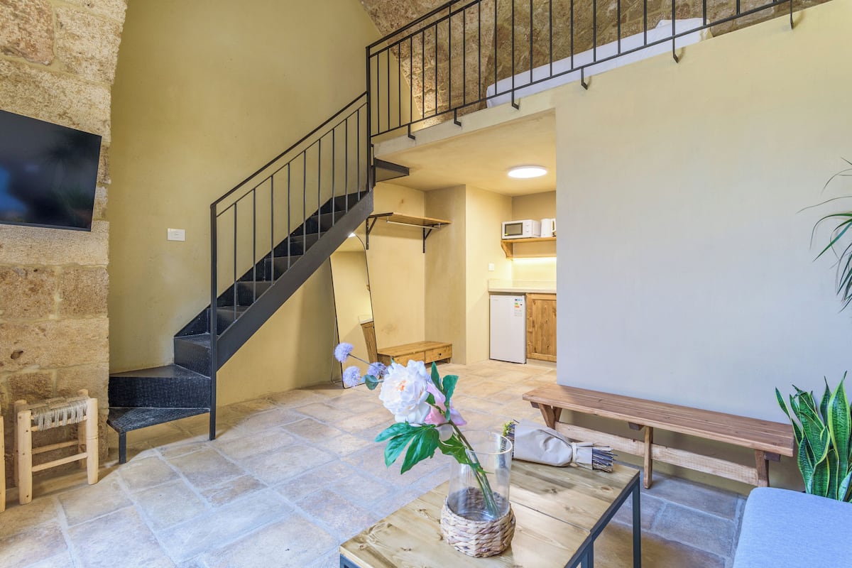Un vaste espace de vie agrémenté d’un mur en pierre, d’un escalier, d’un banc en bois, d’une table à manger et d’une plante en pot.