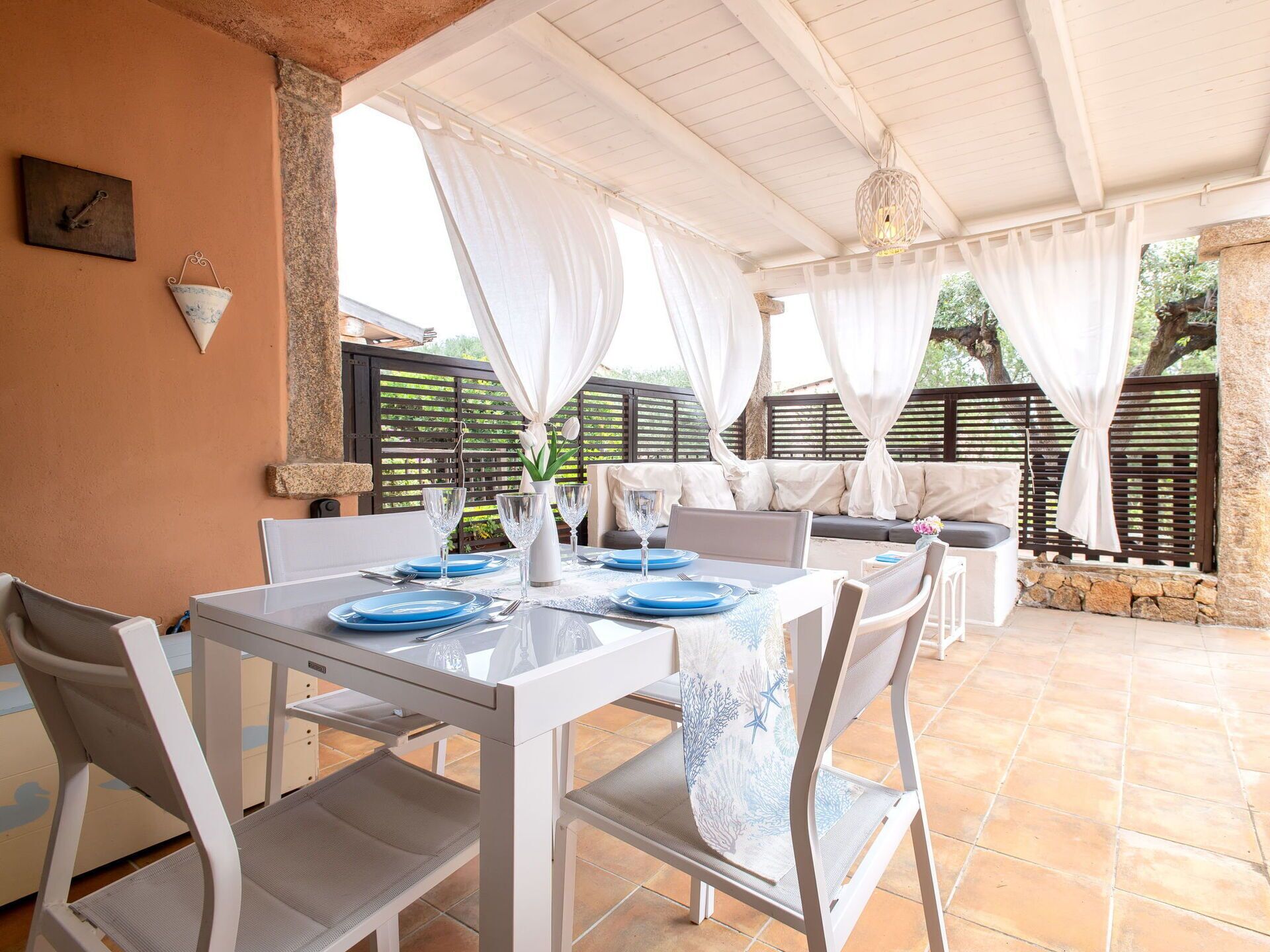 An outdoor patio with a white table set for dining, surrounded by white chairs.