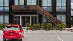 A modern building with a sign for 12th Avenue Suites, featuring a staircase and a red car parked in front.