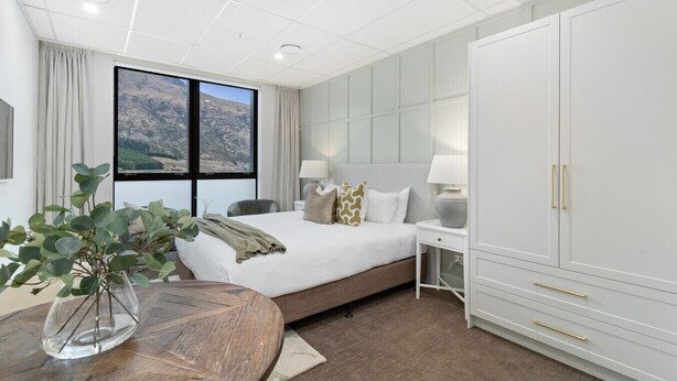 A hotel room with a bed, bedside tables, a wardrobe, and a view of a mountainous landscape through the window.