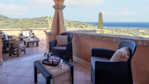 A terrace with wicker furniture, a table with a tray of cups and a teapot, and a view of the sea and hills. - Cosy apartment for 6 guests with A/C, WIFI, TV, patio and pets allowed (Budoni)