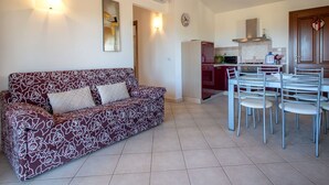 A living room with a sofa, a dining table with chairs, a kitchen area with a stove and microwave, and a clock on the wall. - Cosy apartment for 6 guests with A/C, WIFI, TV, patio and pets allowed (Budoni)