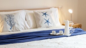 A neatly made bed with a white quilt, two pillows with star designs, a blue blanket, and a bedside table with a white lamp and a tray with cups and a pitcher. - Cosy apartment for 6 guests with A/C, WIFI, TV, patio and pets allowed (Budoni)