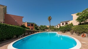 Una piscina rodeada de edificios, un flotador salvavidas y una palmera.