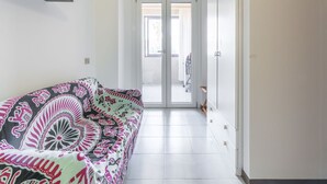 Un pasillo con un sofá estampado, una puerta que da a un balcón y un equipo de aire acondicionado en la pared.