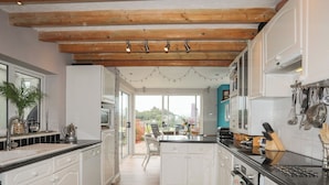 A modern kitchen with white cabinets, wooden flooring, and a view to the outside. - Alltwen (Porthmadog)